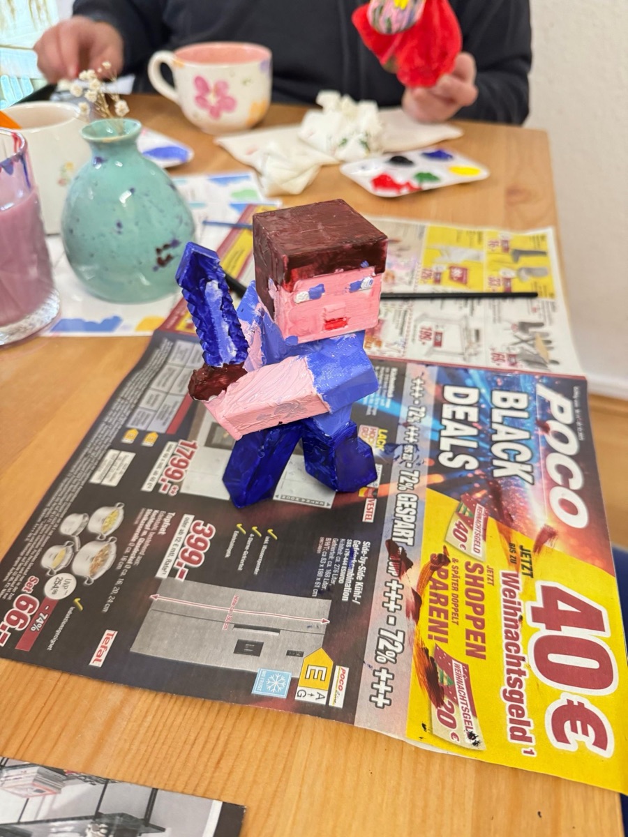 Pixel-style figure with a blue sword painted by a child, on newspaper at a painting table