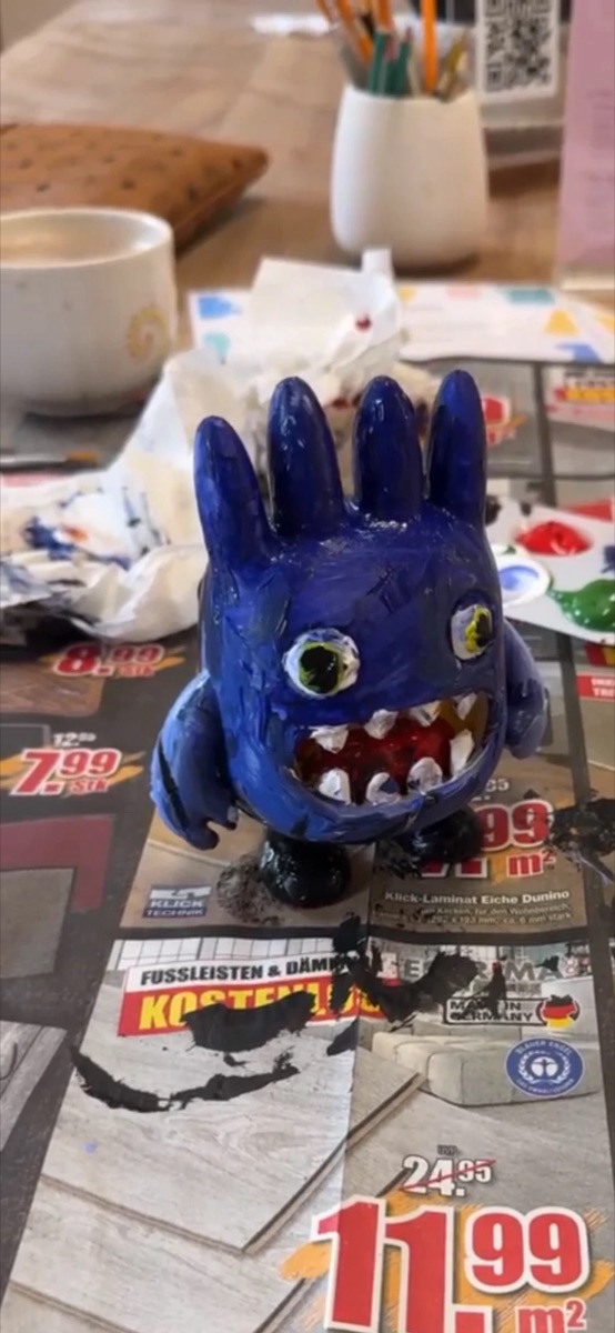 Blue one-eyed monster with white teeth painted by a child, on newspaper